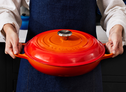 hands of older person help child's hands stir a flame orange pot